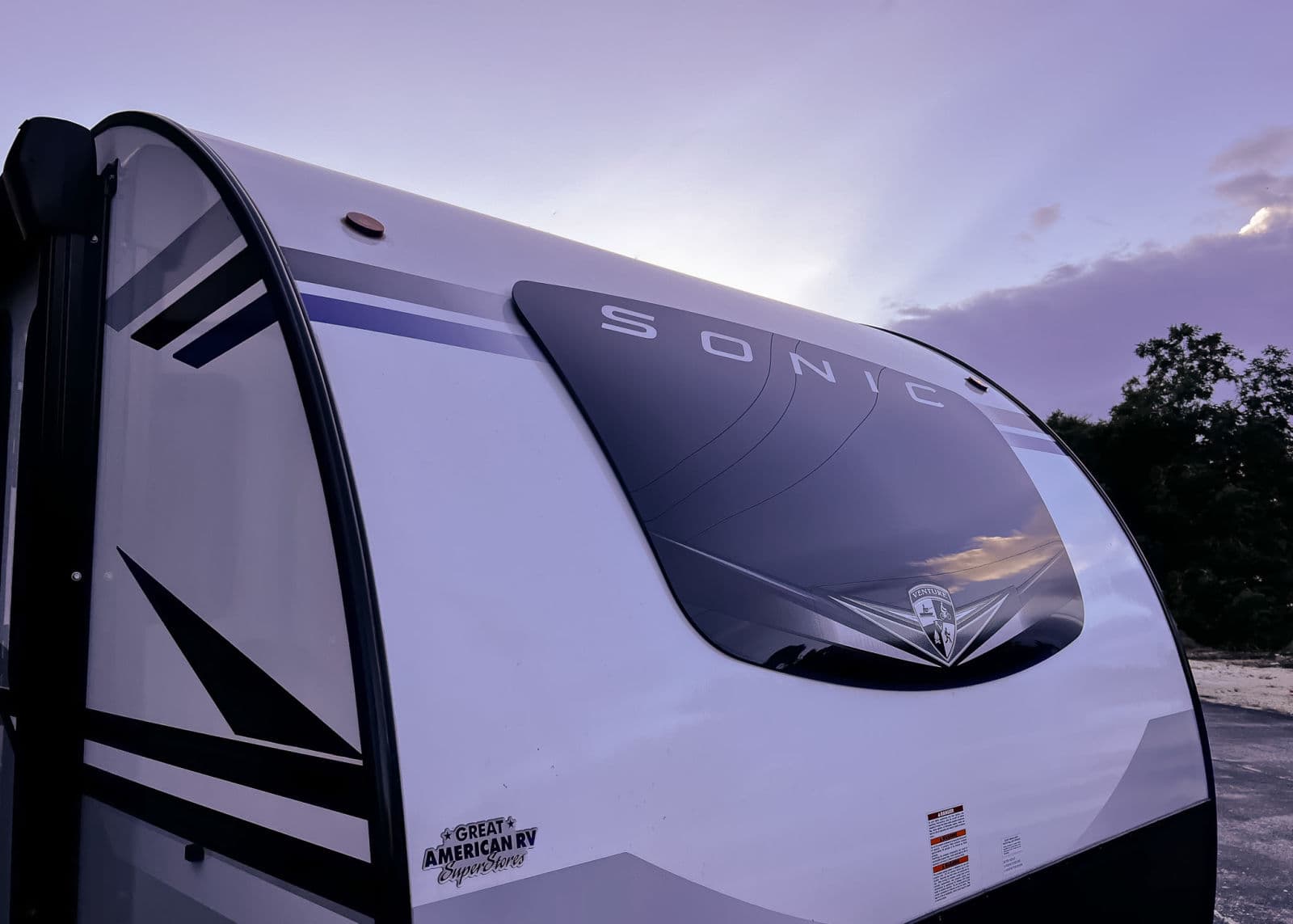 Front view of a white Sonic travel trailer, an excellent RV rental option, under a soft twilight sky.