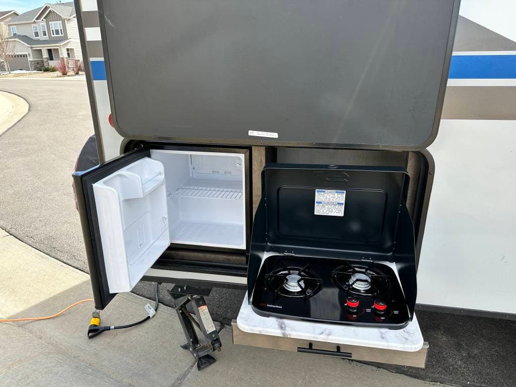 This RV rental features an outdoor kitchen with an open mini-fridge and a two-burner gas stove, perfect for meals on the go.