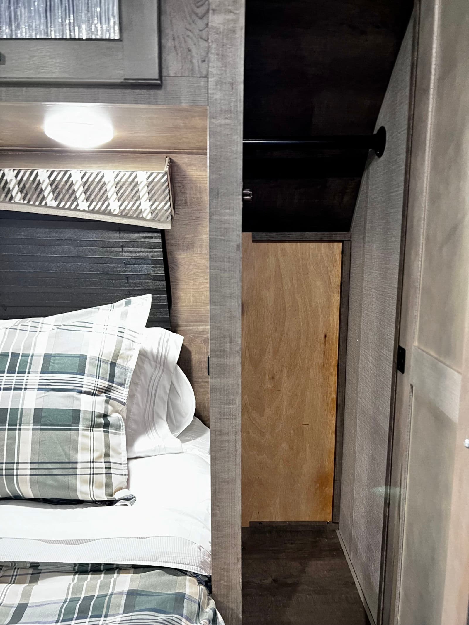 RV rental bedroom interior with a neatly made bed, plaid bedding, and an open closet featuring a wooden back panel.