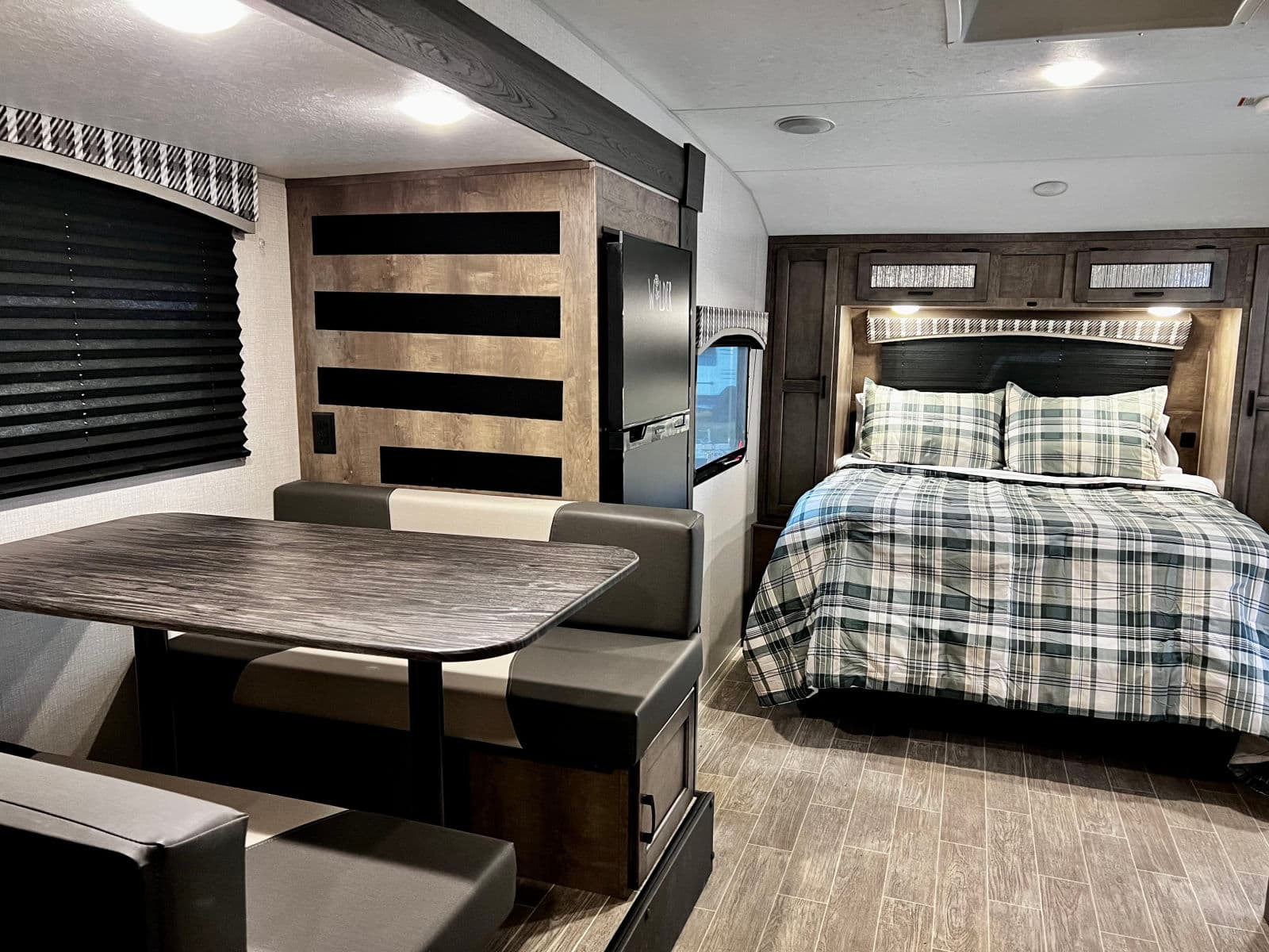 Modern RV rental interior with a comfortable dinette and plaid-covered bed, ideal for travel trailer vacations.