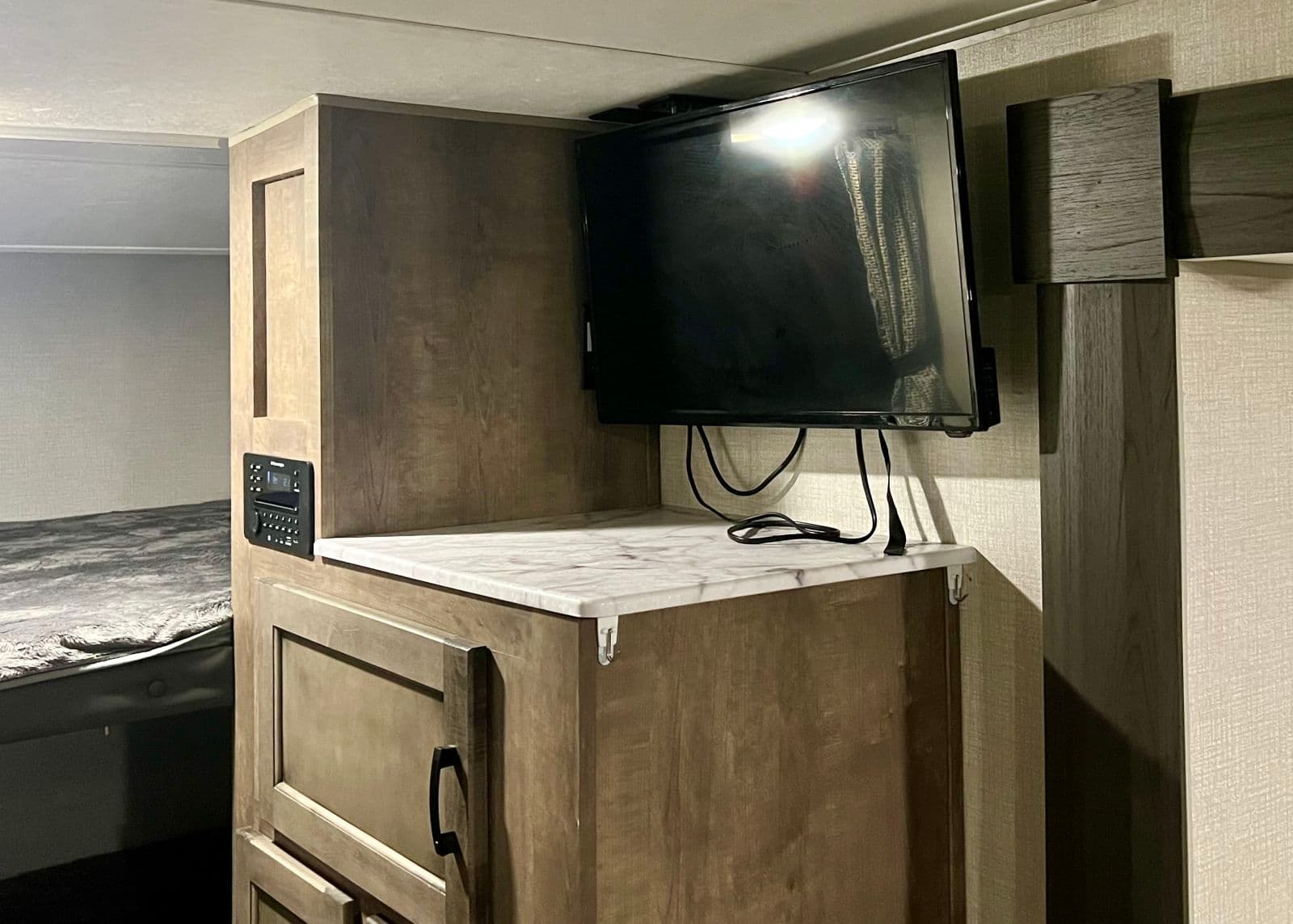 Enjoy entertainment in your RV rental! Cozy interior with TV, storage cabinet, control panel, and sleeping area.