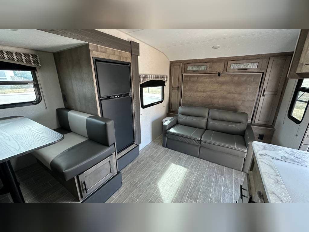 RV rental interior: dining booth, fridge, and a sofa fronting a fold-down bed. Modern and ready for travel.
