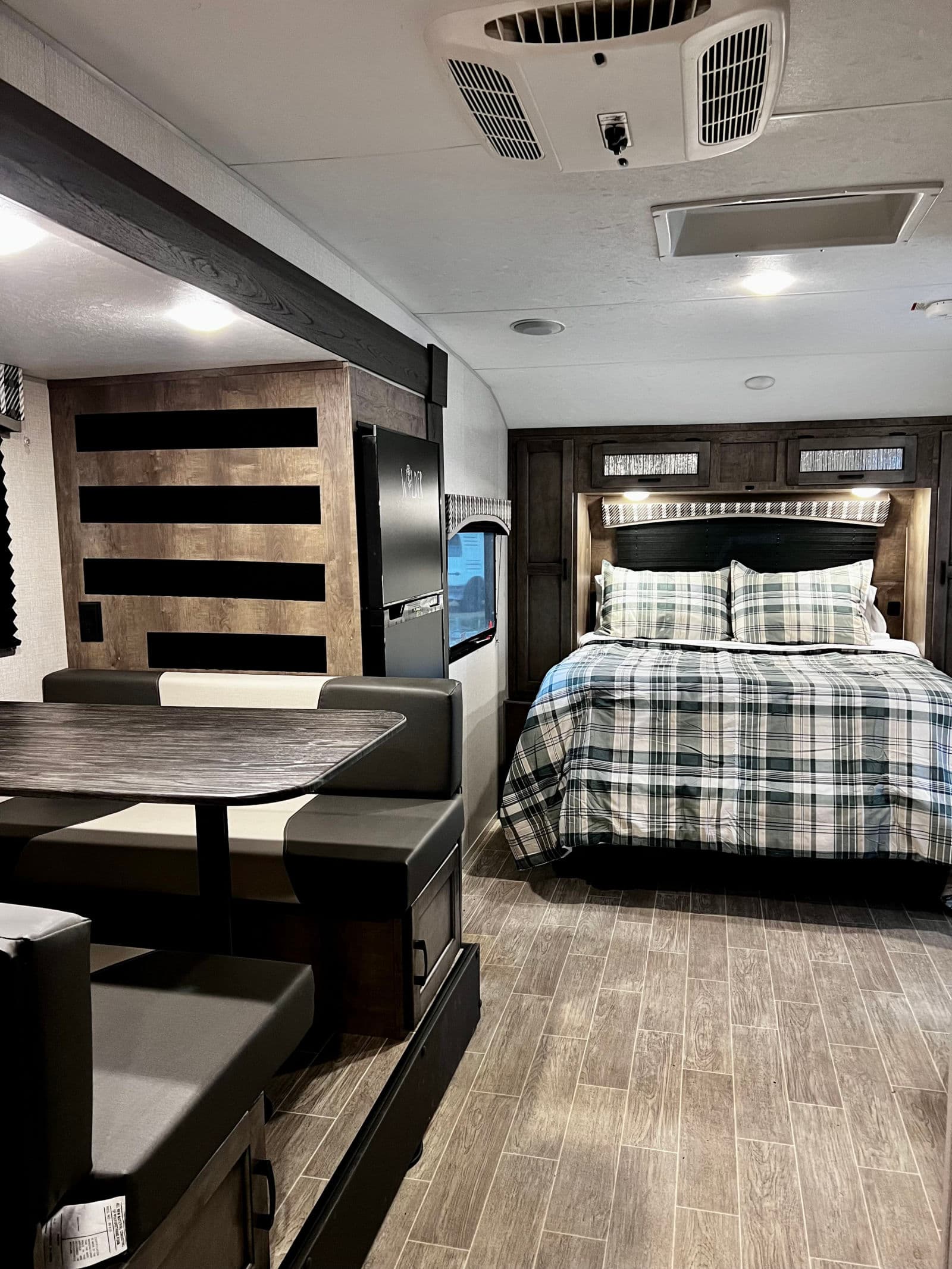 Modern RV rental interior featuring a cozy dinette, a comfortable bedroom with plaid bedding, and stylish wood accents.