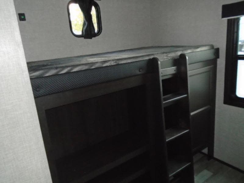 This RV rental features bunk beds with mattresses, a ladder for the upper bunk, and windows in a compact sleeping space.