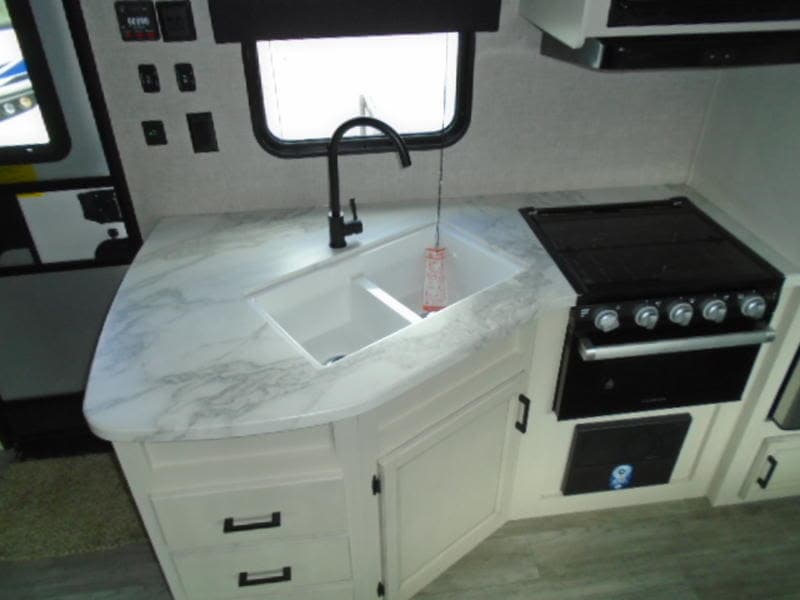 RV rental kitchen featuring a white marble-look counter, black faucet, double sink, and a stove/oven combo. Perfect for travel.