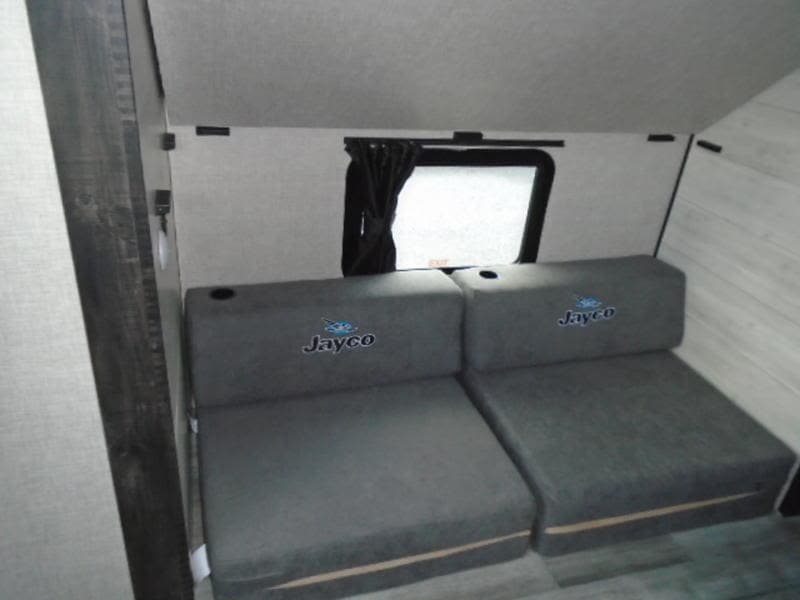 RV rental interior featuring two gray Jayco seats with cup holders and a small window, providing comfortable living space.