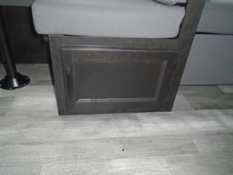 RV rental interior view: Close-up of a dark wood dinette cabinet with a grey cushion and wood-look flooring.