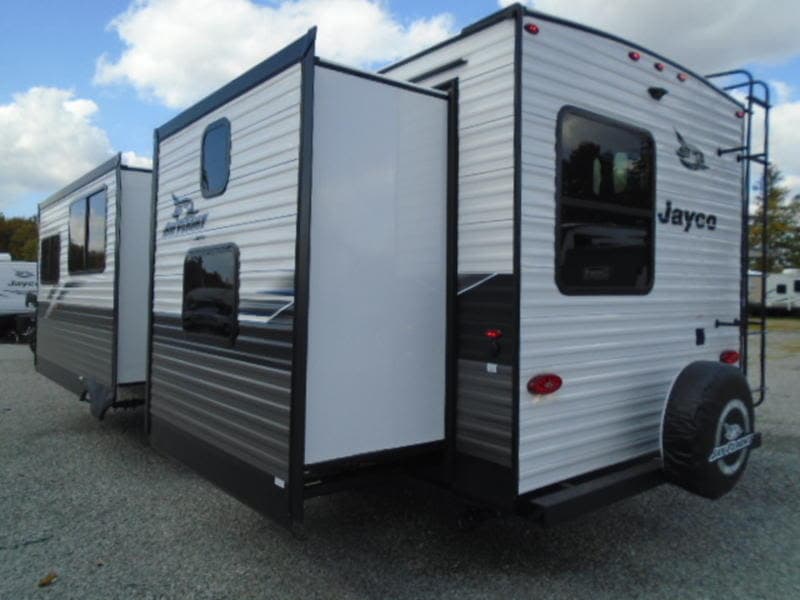 This Jayco travel trailer rv rental, with extended slide-outs, rear ladder, and spare tire, is parked on gravel.