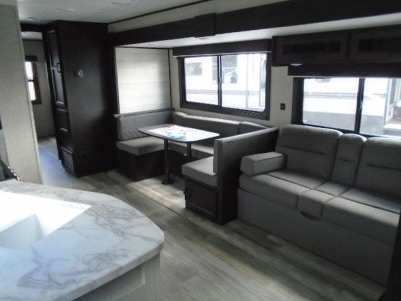 This RV rental's inviting interior features a U-shaped dinette, comfortable sofa, and bright windows, ideal for travel.