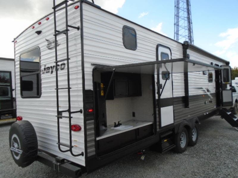 RV rental: Modern travel trailer with rear ladder, spare tire, and fully equipped outdoor kitchen under an awning.