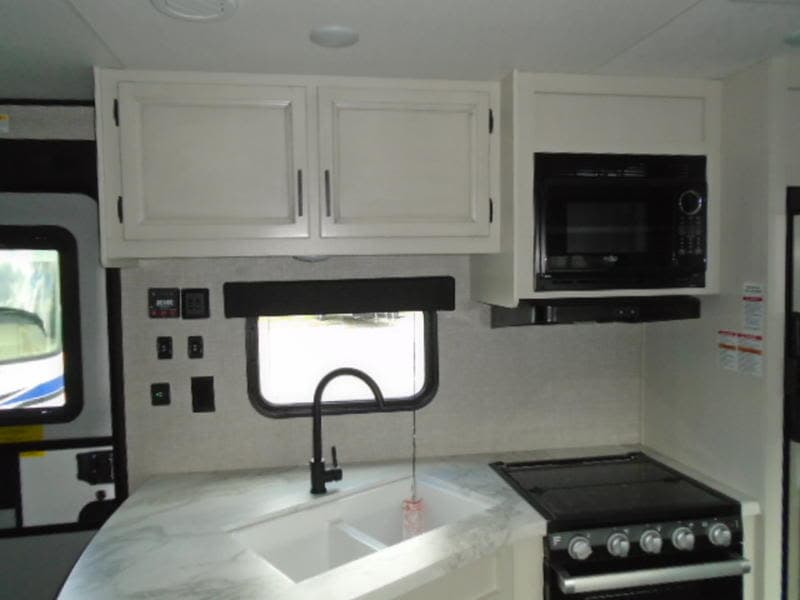 This rv rental kitchen features white cabinets, a microwave, sink, faucet, and stovetop, ready for your adventures.