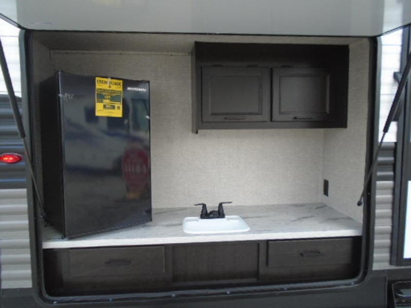 Enjoy this RV rental's outdoor kitchen! Features a mini-fridge, sink, countertop, and cabinets for convenient camping.
