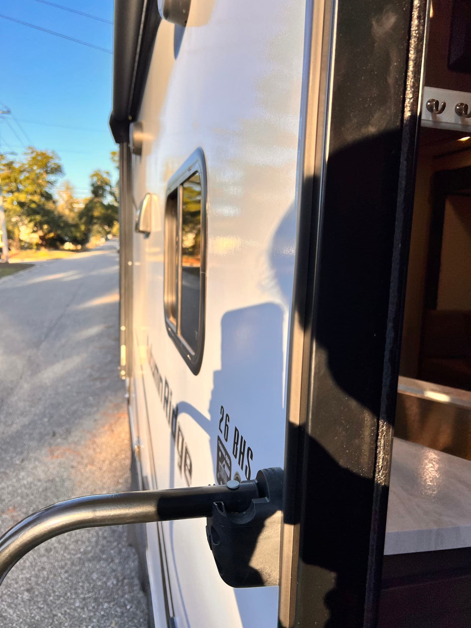 Sunlit RV rental: the 26 BHS travel trailer's open doorway, handrail, and exterior. Glimpse of the cozy interior.