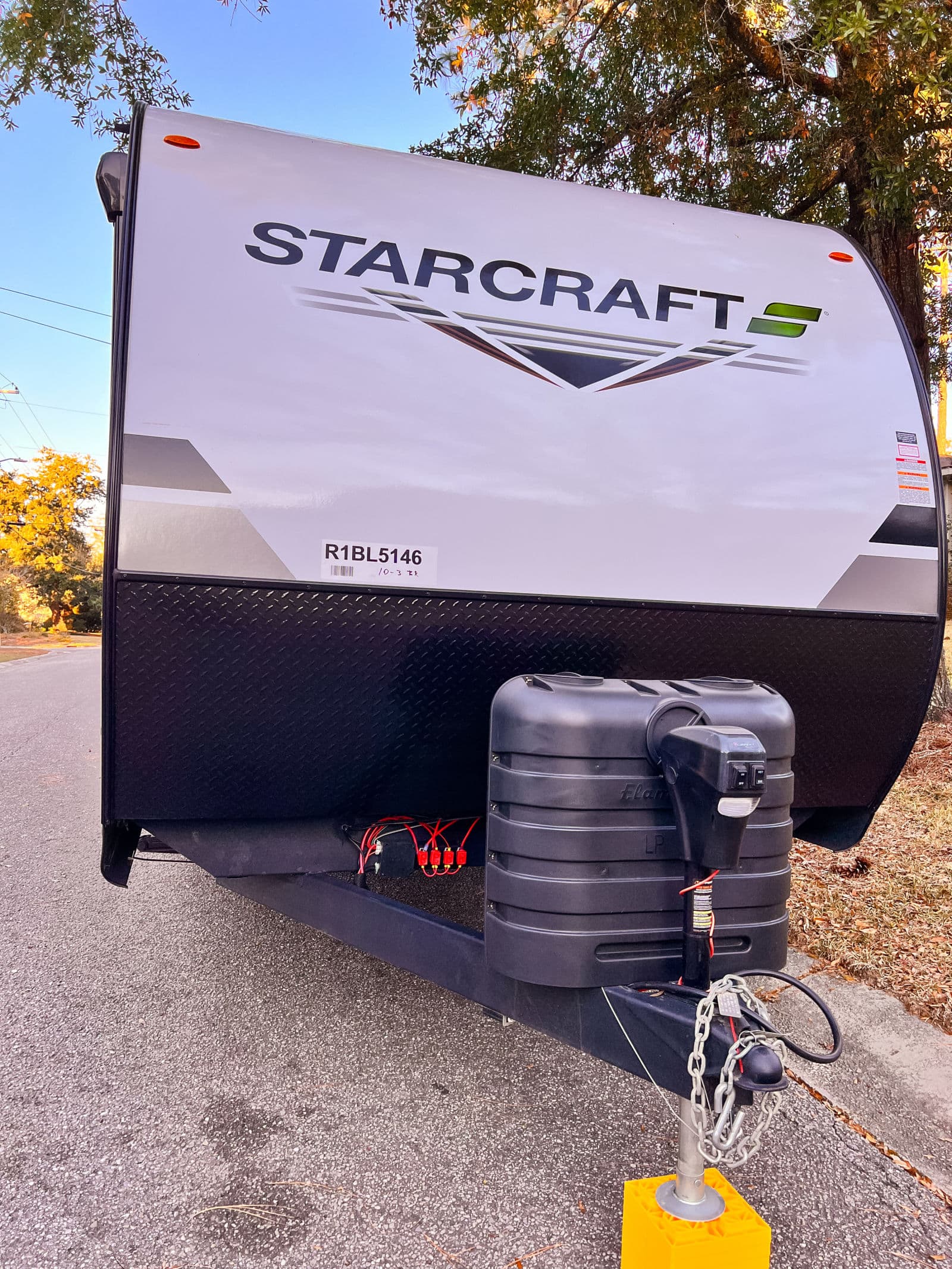 Front view of a Starcraft travel trailer, perfect for an RV rental, highlighting the propane tank and hitch assembly.