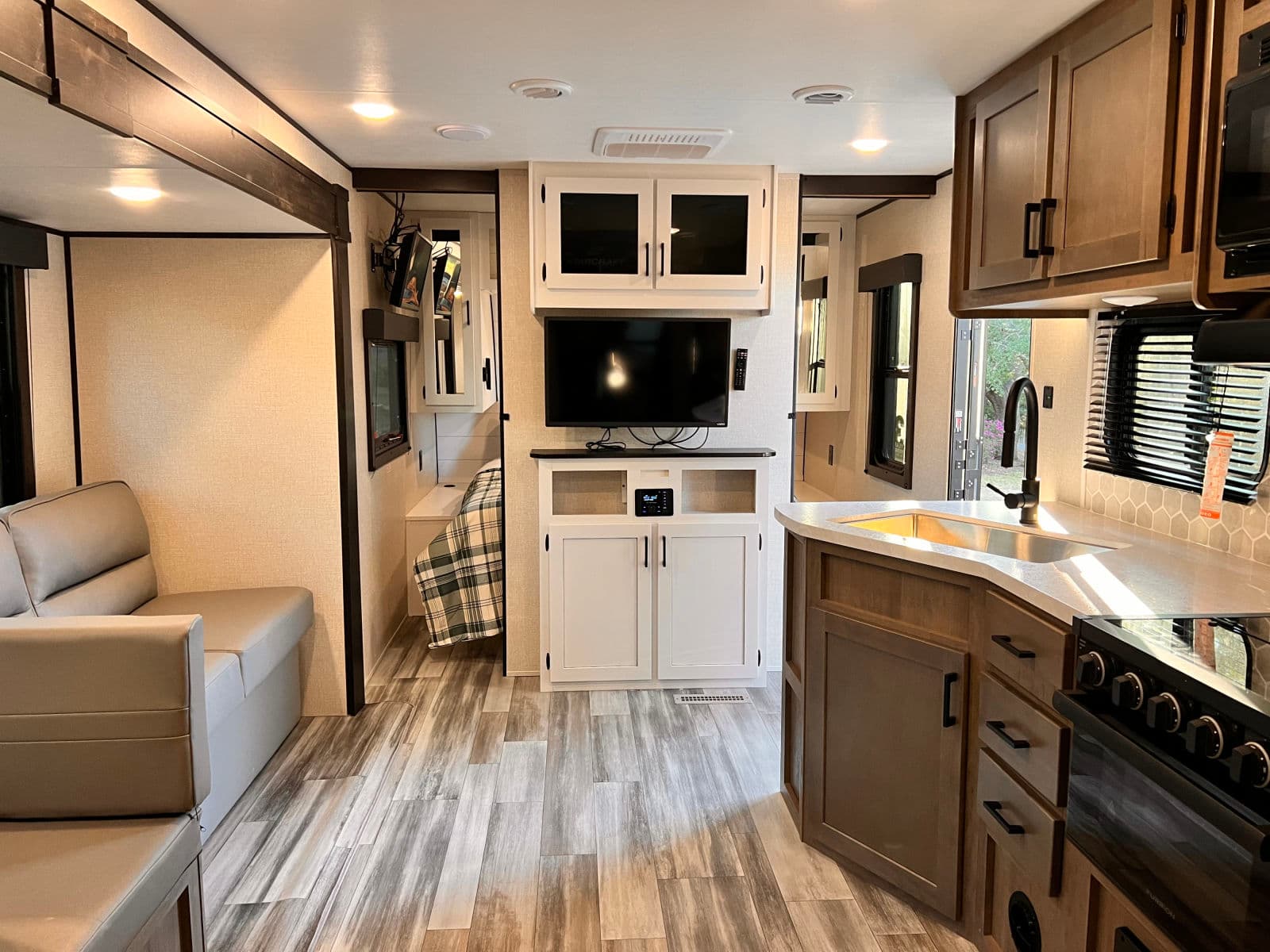 Modern RV rental showcasing a living space, kitchen with stove & sink, and an accessible bedroom, featuring wood-look flooring.