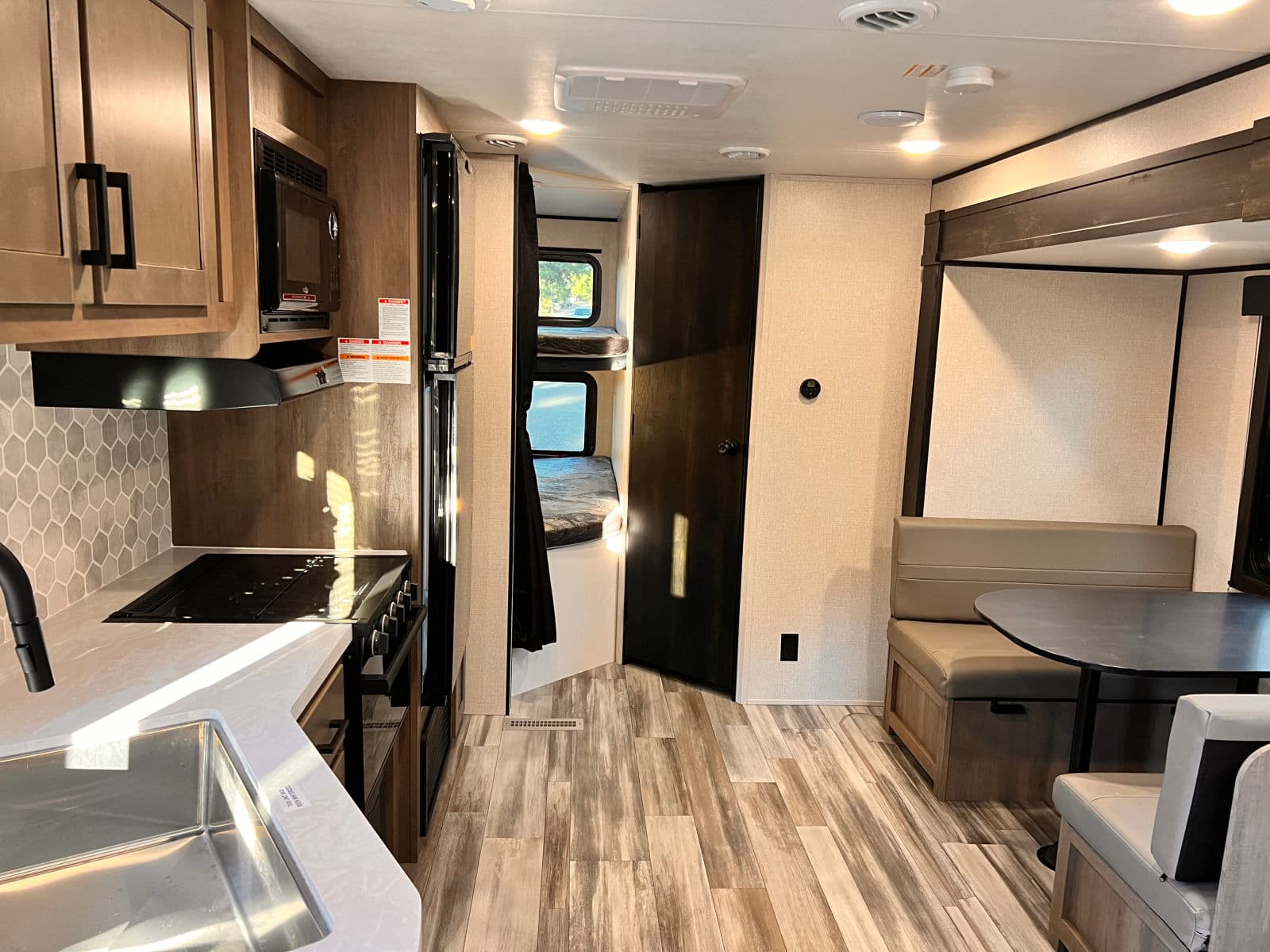 RV rental interior showcasing a full kitchen with sink/stove, a cozy dinette, and private bunk beds. Modern and functional space.