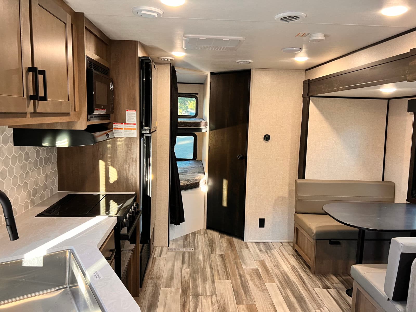 Modern RV rental interior showcasing a kitchen, dining booth, and bunk beds, featuring a bright, functional layout.