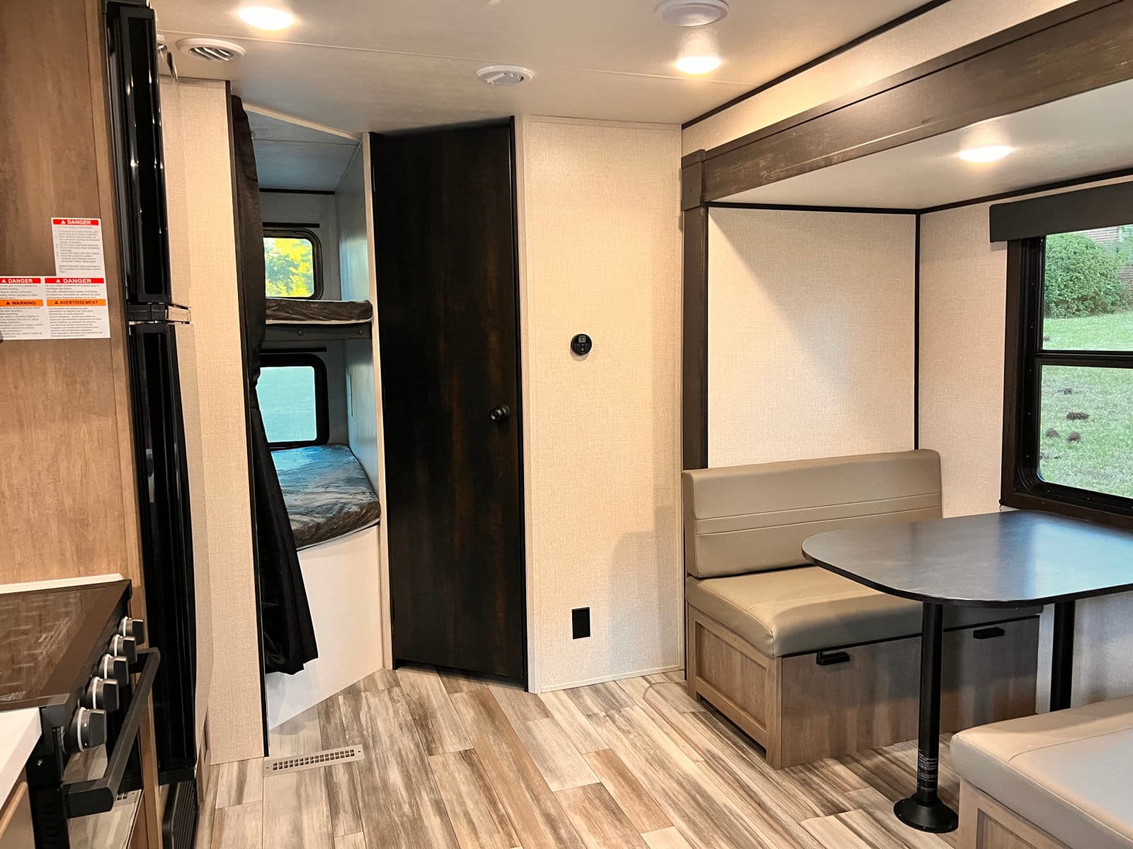 Spacious RV rental interior with dinette, bunk beds, and kitchen area, featuring wood-look flooring and light walls.