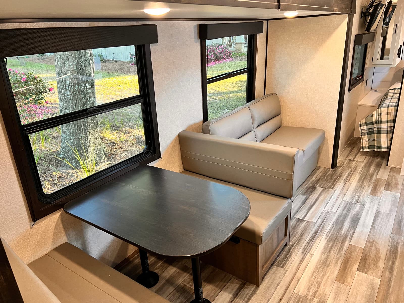 Cozy RV rental interior: dinette with table & bench seating, sofa, and bright windows offering outdoor views.