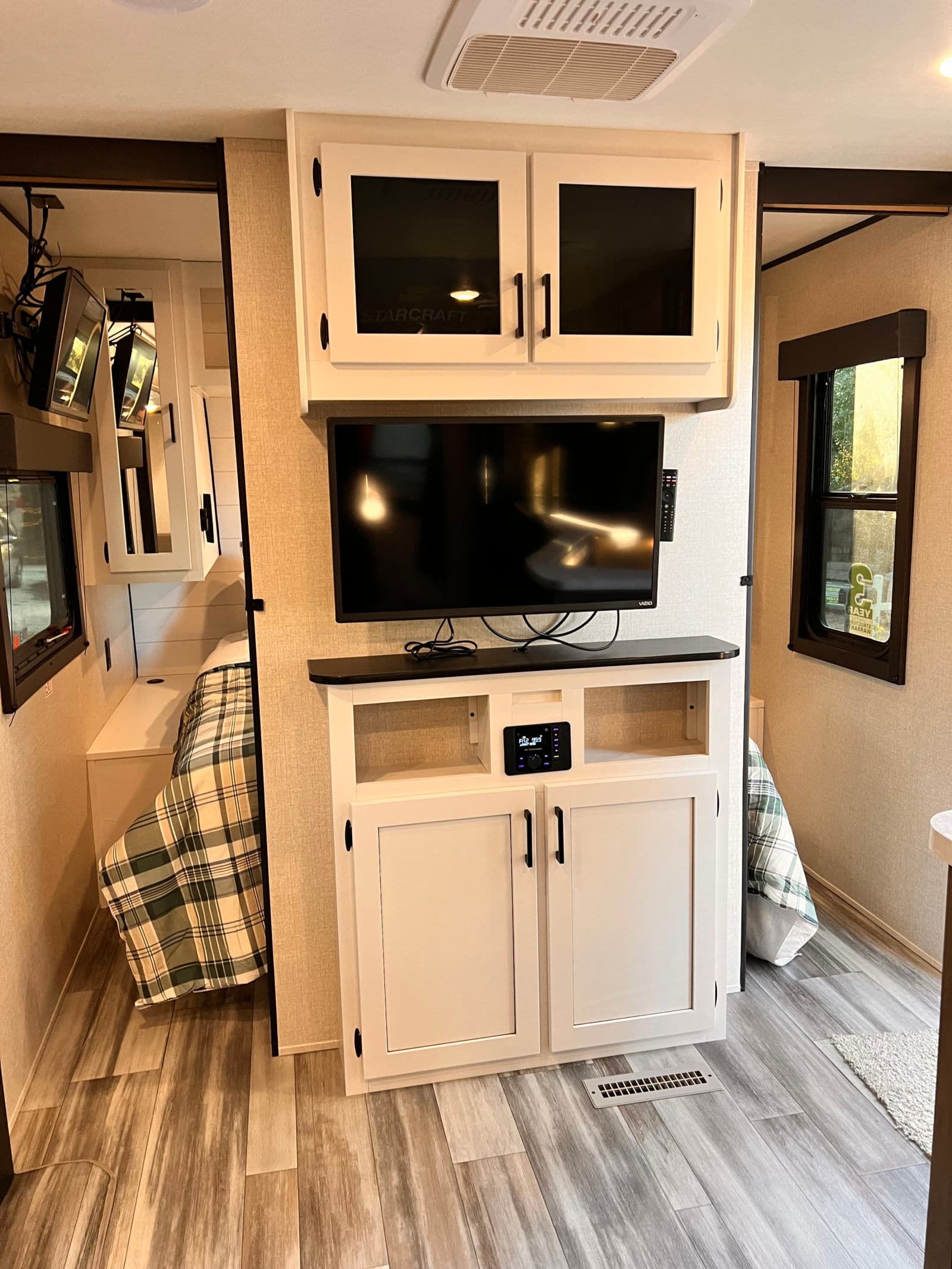 Inside this RV rental: a modern entertainment center with TV, overhead cabinets, and a cozy bedroom nook.