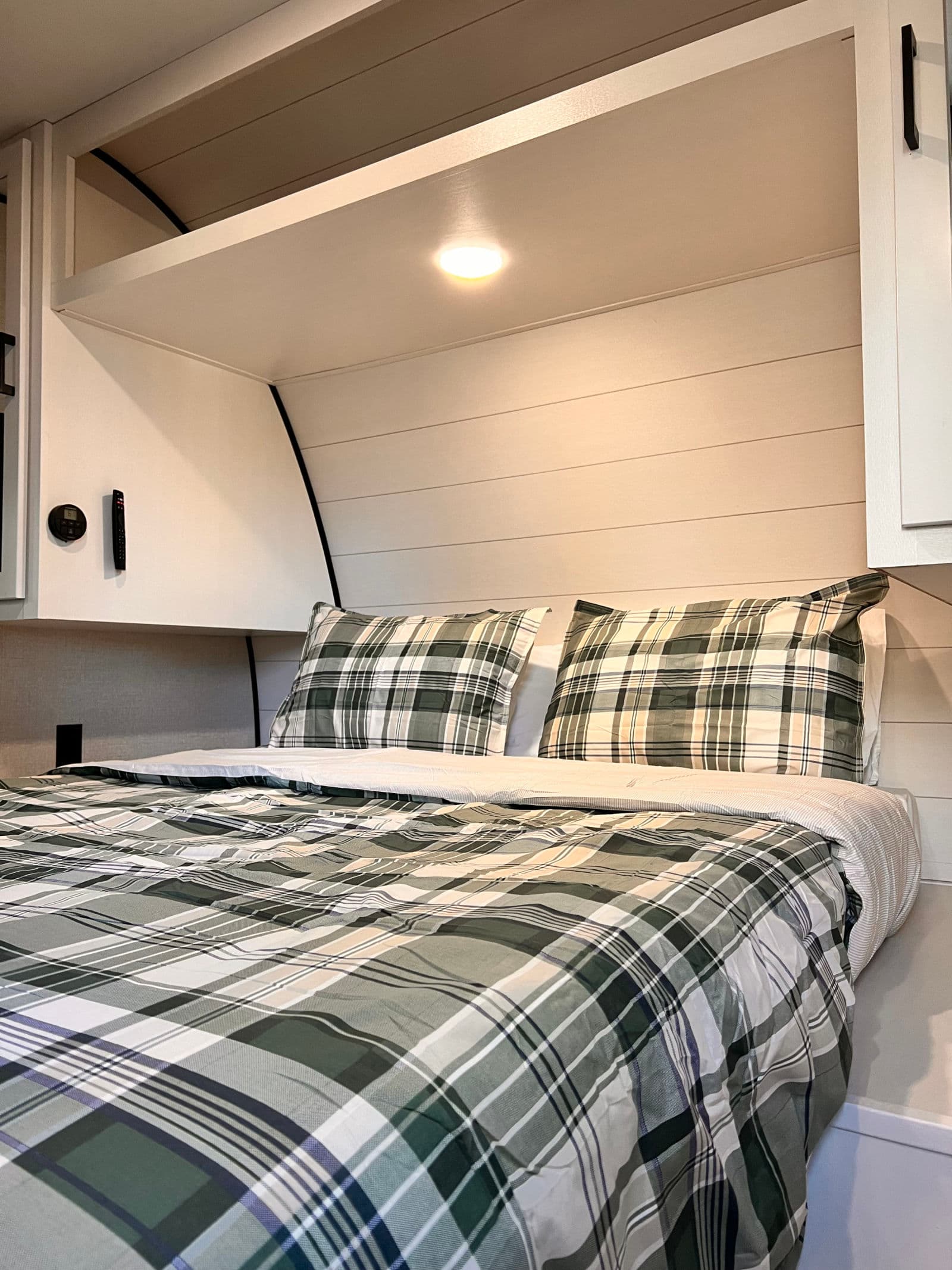 Cozy RV rental bedroom with green plaid bedding, shiplap walls, bright overhead light, and handy storage cabinets.