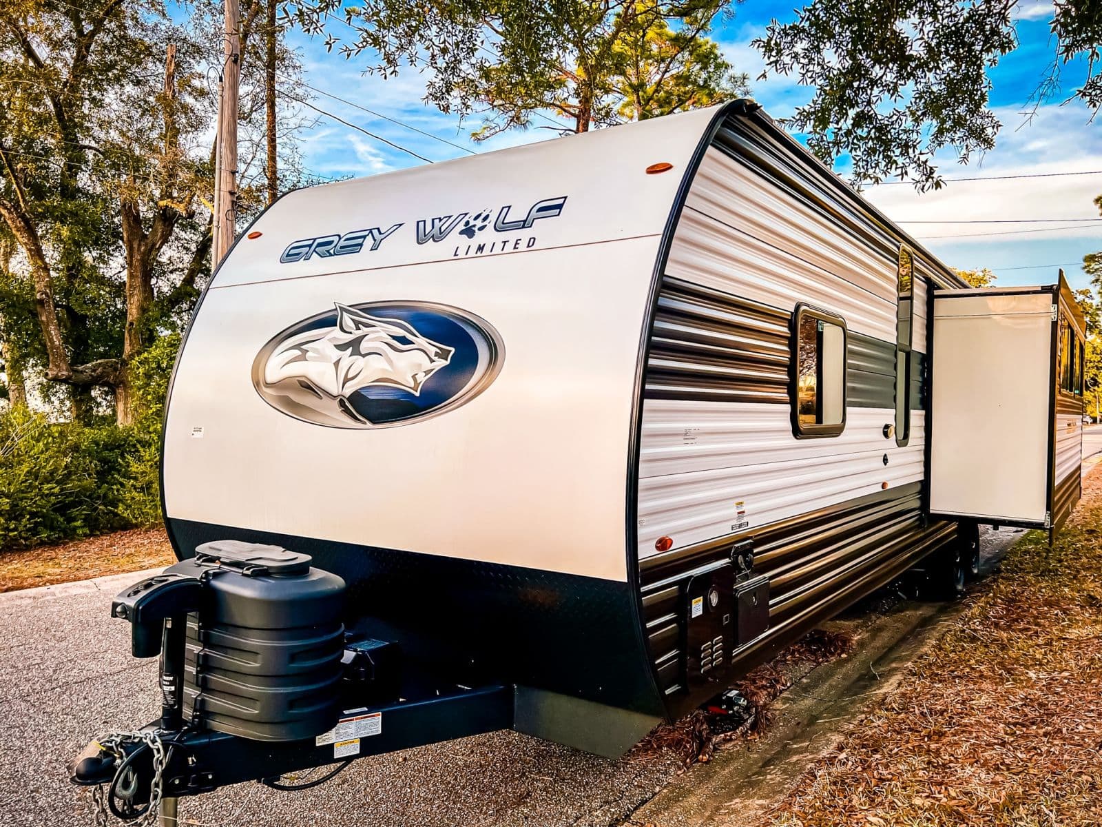 Discover this Grey Wolf Limited rv rental! This white and dark grey travel trailer, featuring a prominent wolf logo, is parked outdoors.
