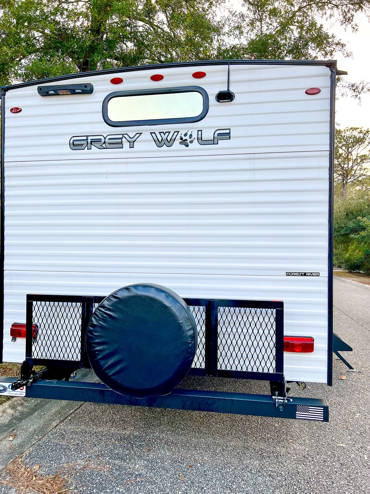Rear view of a white Grey Wolf travel trailer rv rental. Features a spare tire, cargo rack, and Forest River logo.