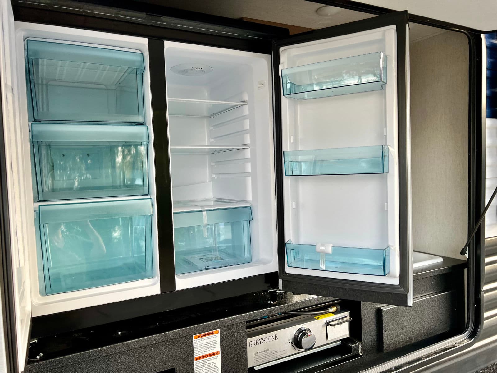 RV rental outdoor kitchen with an open mini-fridge, freezer drawers, Greystone grill, and a small sink for convenience.