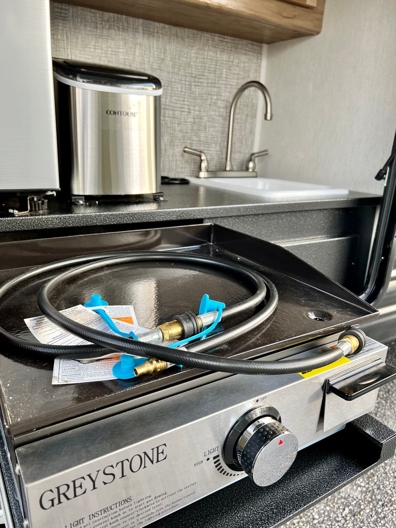 This RV rental's outdoor kitchen features a Greystone griddle, gas hose, Contoure appliance, and sink.
