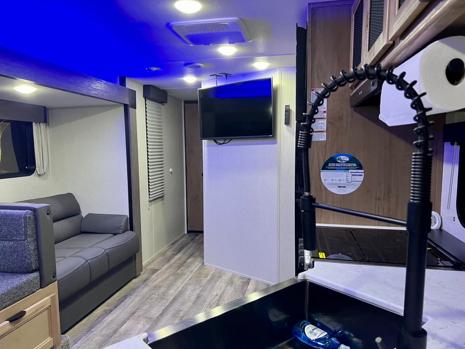 Explore this modern RV rental interior featuring a living area with a gray sofa, bunk area, TV, and kitchen with a flexible faucet.