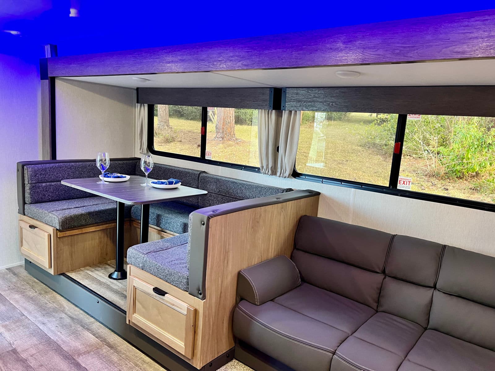 Modern RV rental interior: a comfy dinette, sofa, and scenic views under ambient blue lighting.