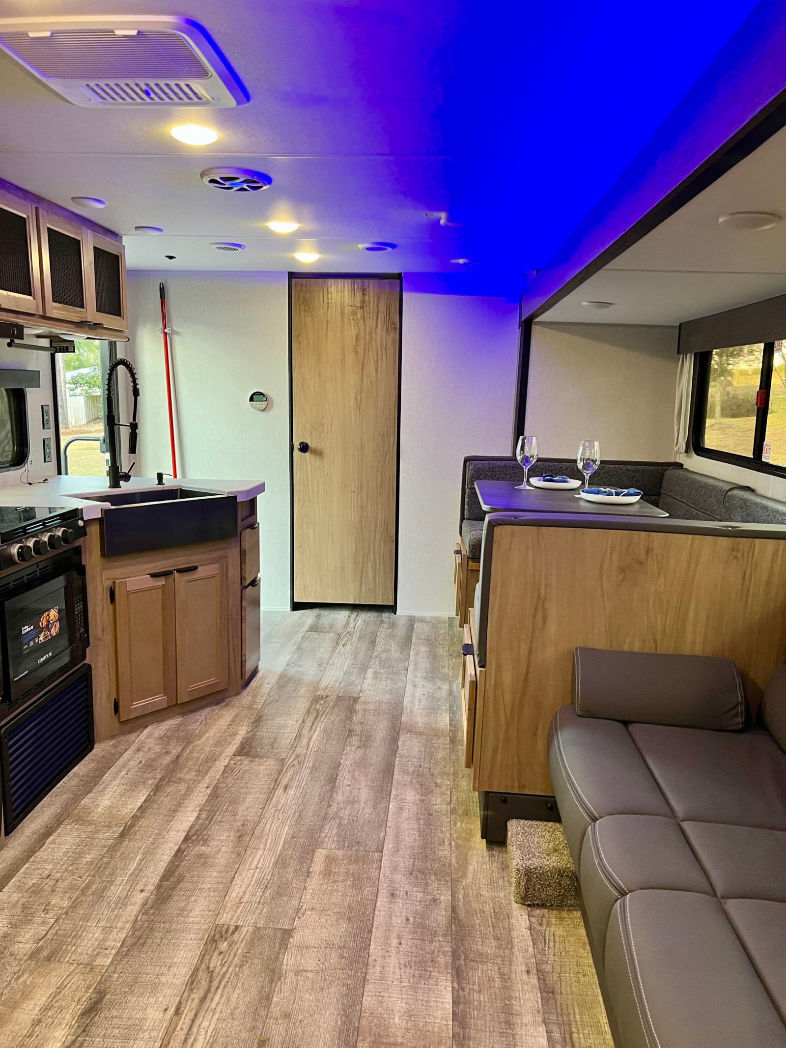 Rv rental interior: sleek kitchen with farmhouse sink, dining booth, and living area. Blue ceiling lights add modern flair.