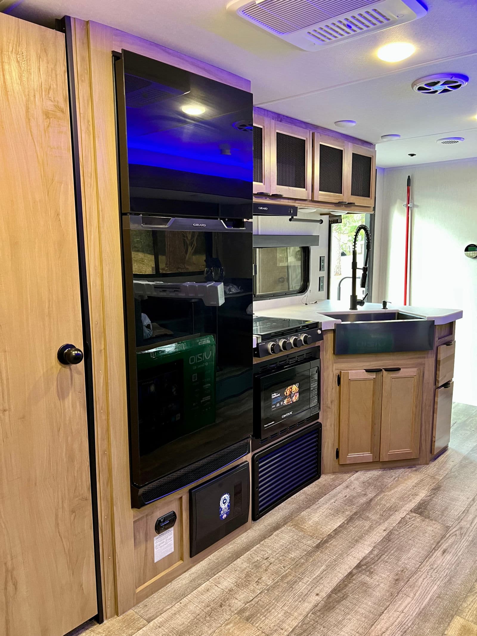 Modern rv rental kitchen with sleek black appliances: a large refrigerator, stove, microwave, farmhouse sink, and wood cabinets.