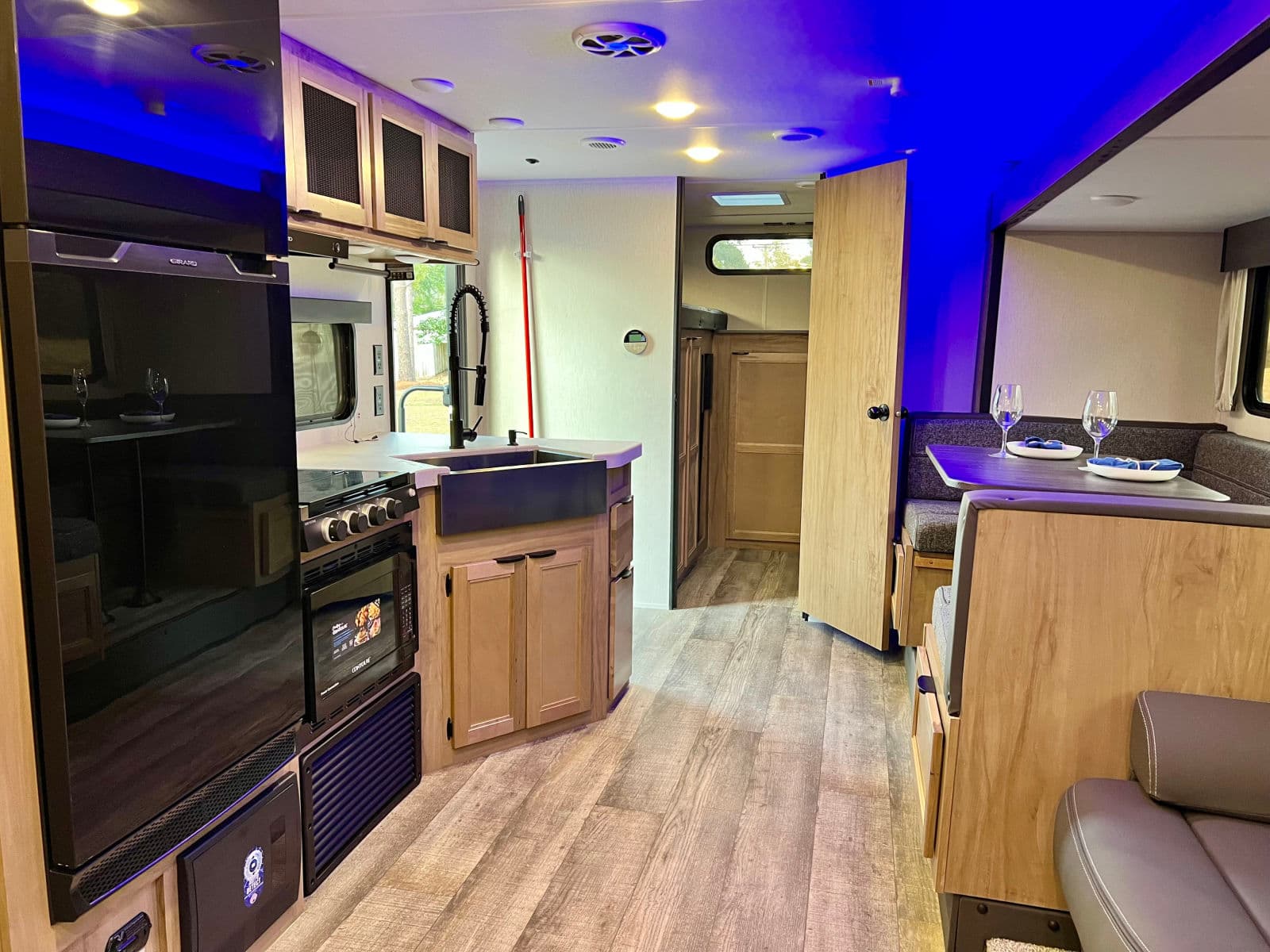 Relaxing rv rental interior: kitchen with farm sink, dining booth, wood floor, and atmospheric blue lighting.