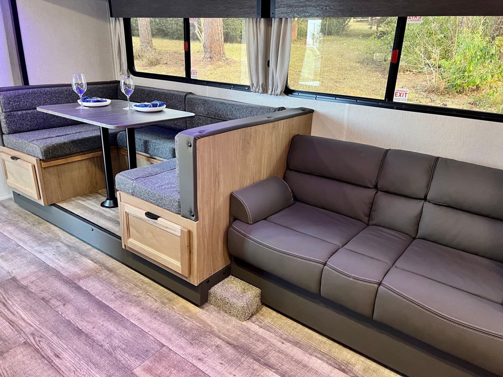 This inviting RV rental interior features a cozy dinette with seating, a sofa for lounging, and practical wood-look flooring.