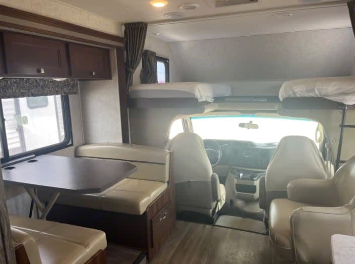 Spacious rv rental interior showing dining area, bunk beds, and driver's cabin for comfortable travel.