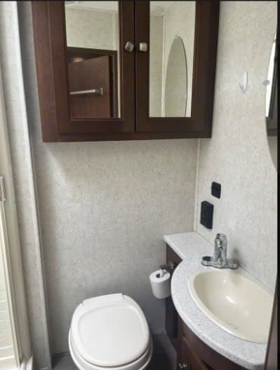 RV rental bathroom features a compact toilet, sink, and mirrored medicine cabinet, ideal for travel.