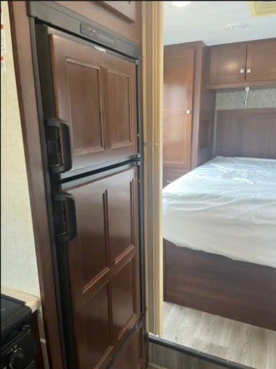 RV rental: View of a wood-paneled Dometic refrigerator leading to a comfortable RV bedroom with a bed and built-in cabinets.