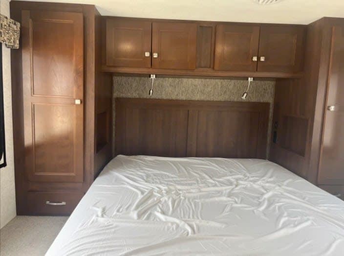RV rental bedroom with a bed, wood headboard, overhead cabinets, and side wardrobes for convenient storage.