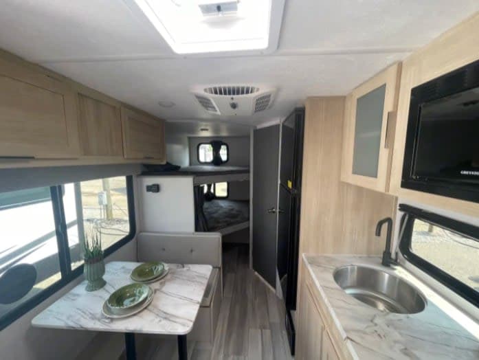 Bright rv rental interior showing a kitchen with sink, dinette seating, and bunk beds for a comfortable travel experience.