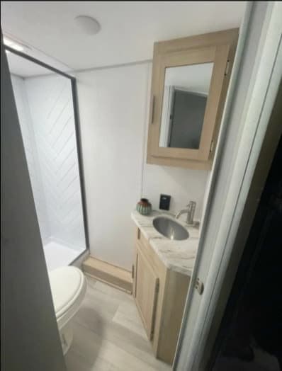 Clean RV rental bathroom features a compact shower, toilet, vanity with sink, and mirrored cabinet.