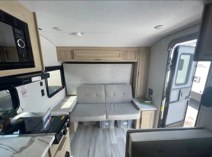This RV rental interior features a compact kitchen, sofa, and convertible sleeping area, ideal for travel and adventure.