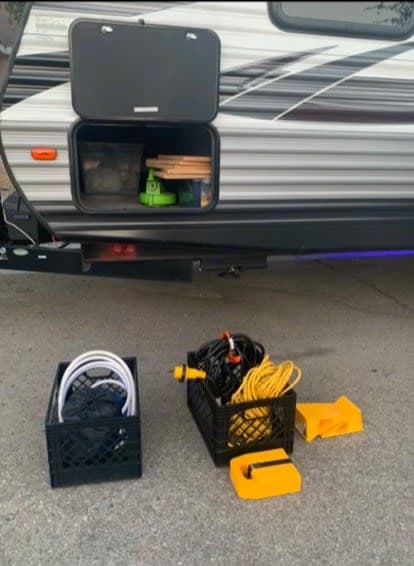RV rental setup. Open compartment reveals blocks. Crates hold water hoses, power cords, and leveling blocks.
