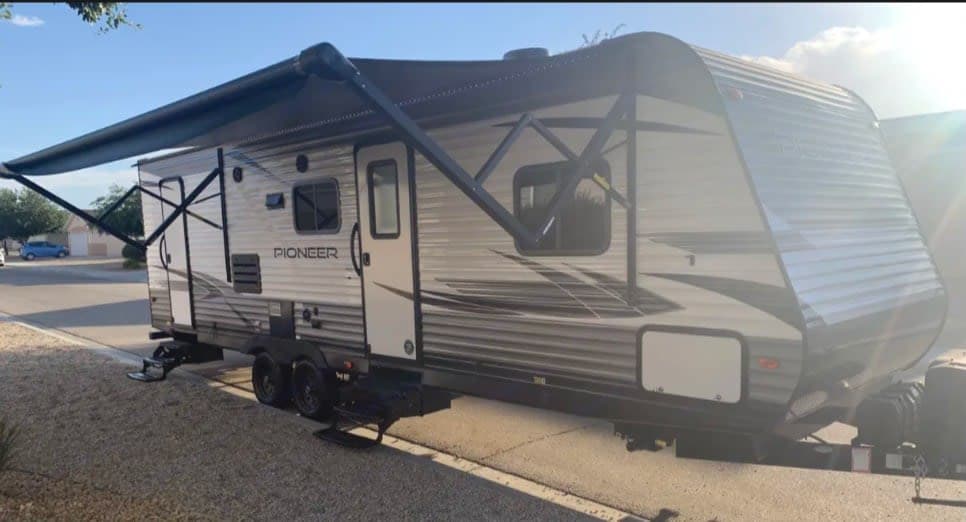 This RV rental image displays a light-colored travel trailer with an extended awning, parked outside on a sunny day.