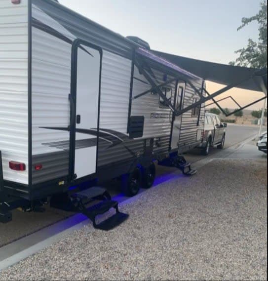 Parked outdoors, this travel trailer rv rental boasts an extended awning & cool blue underglow lighting for evening ambiance.