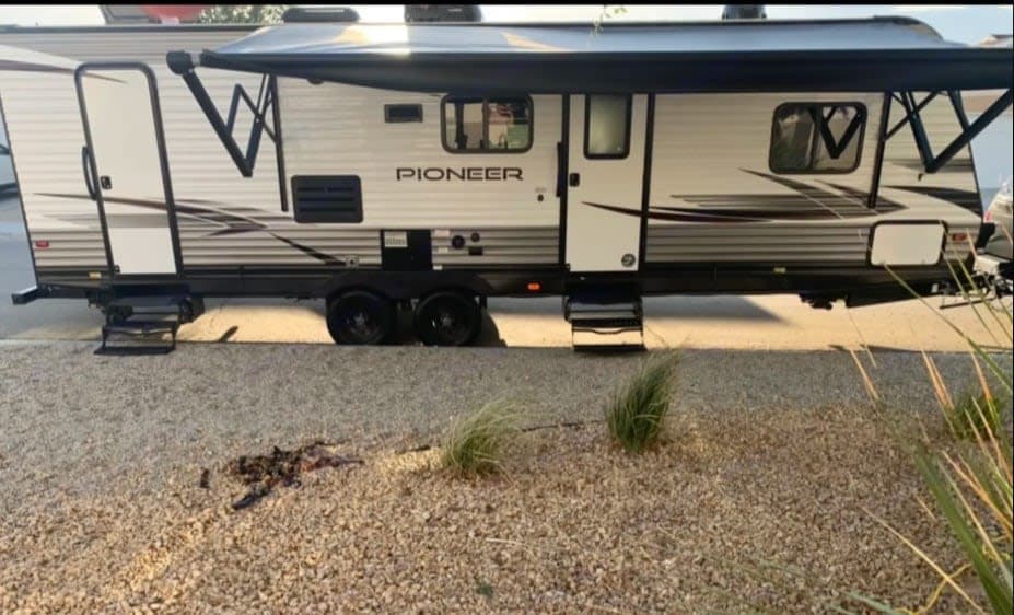 White Pioneer travel trailer, perfect for rv rental, with awning out and steps down on gravel surface.