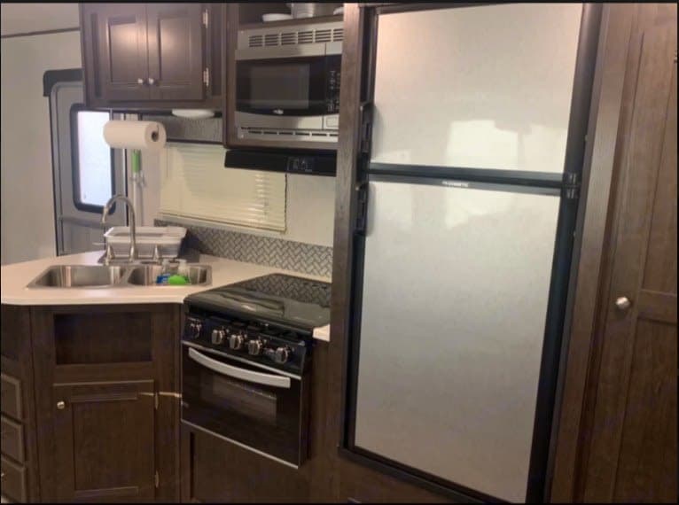A well-equipped rv rental kitchen showing a sink, stove, microwave, and refrigerator for convenient road trips.