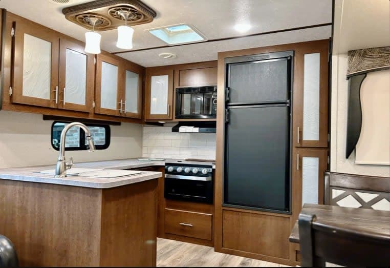 Modern RV rental kitchen featuring wood cabinets, sink, fridge, stove, microwave, and skylight. Ideal for travel adventures.