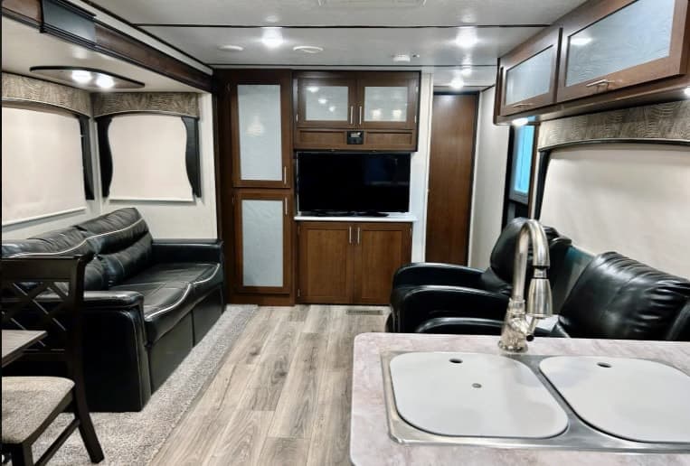 Spacious RV rental interior featuring black leather seating, an entertainment center with TV, and a dual kitchen sink.