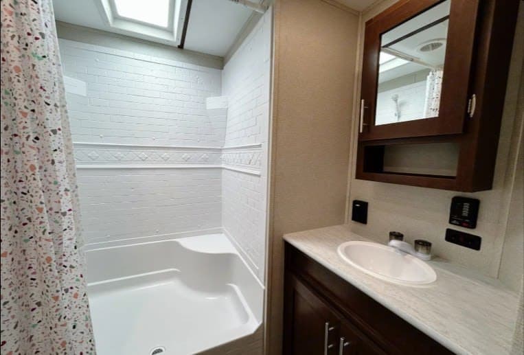 RV rental bathroom with white shower, tub, skylight, and vanity area with sink and mirrored medicine cabinet.